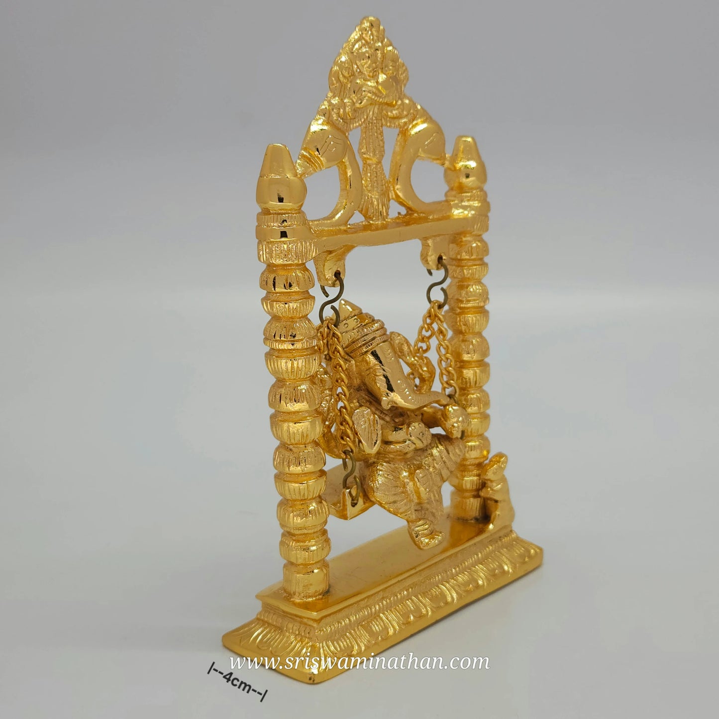 Side view of brass Ganesha statue seated on decorative swing