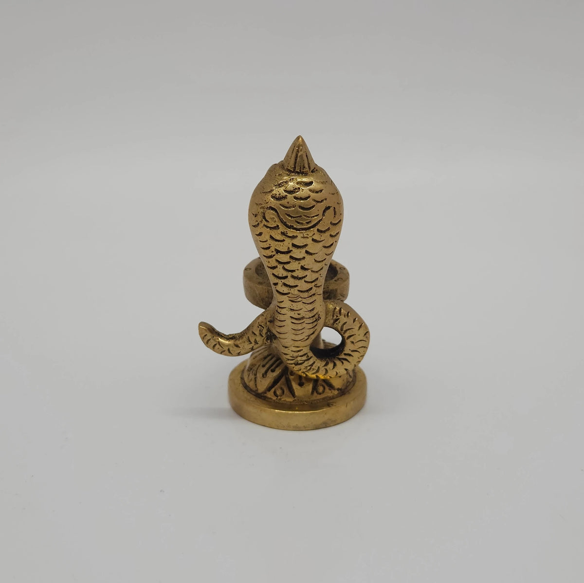 Direct back profile view of the solid cast brass Nagalingam idol showing the coiled serpent body details climbing up toward the canopy hood.