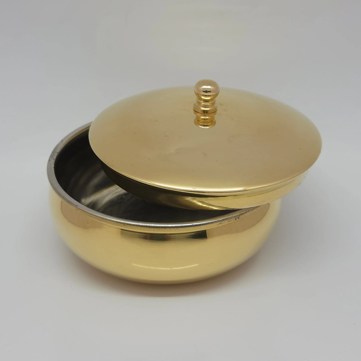 High three-quarter perspective angle view of the brass food serving bowl showing the heavy material depth and golden luster under shop setup lighting.