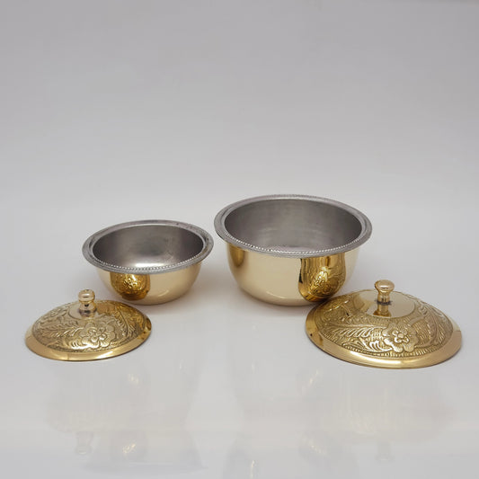 Front view of two sizes of pure brass tin-lined uruli serving bowls with their floral engraved lids placed open on a white surface to show the inner metallic silver lining.