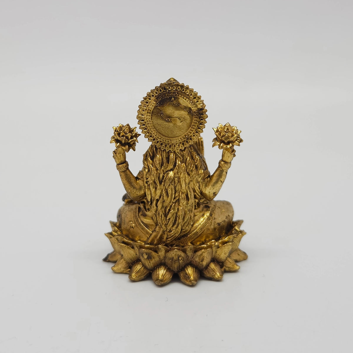 Direct straight back view of the solid brass Lakshmi statue in her real form demonstrating the detailed rear surface of the sunburst halo crown and back hair curls over the round base.