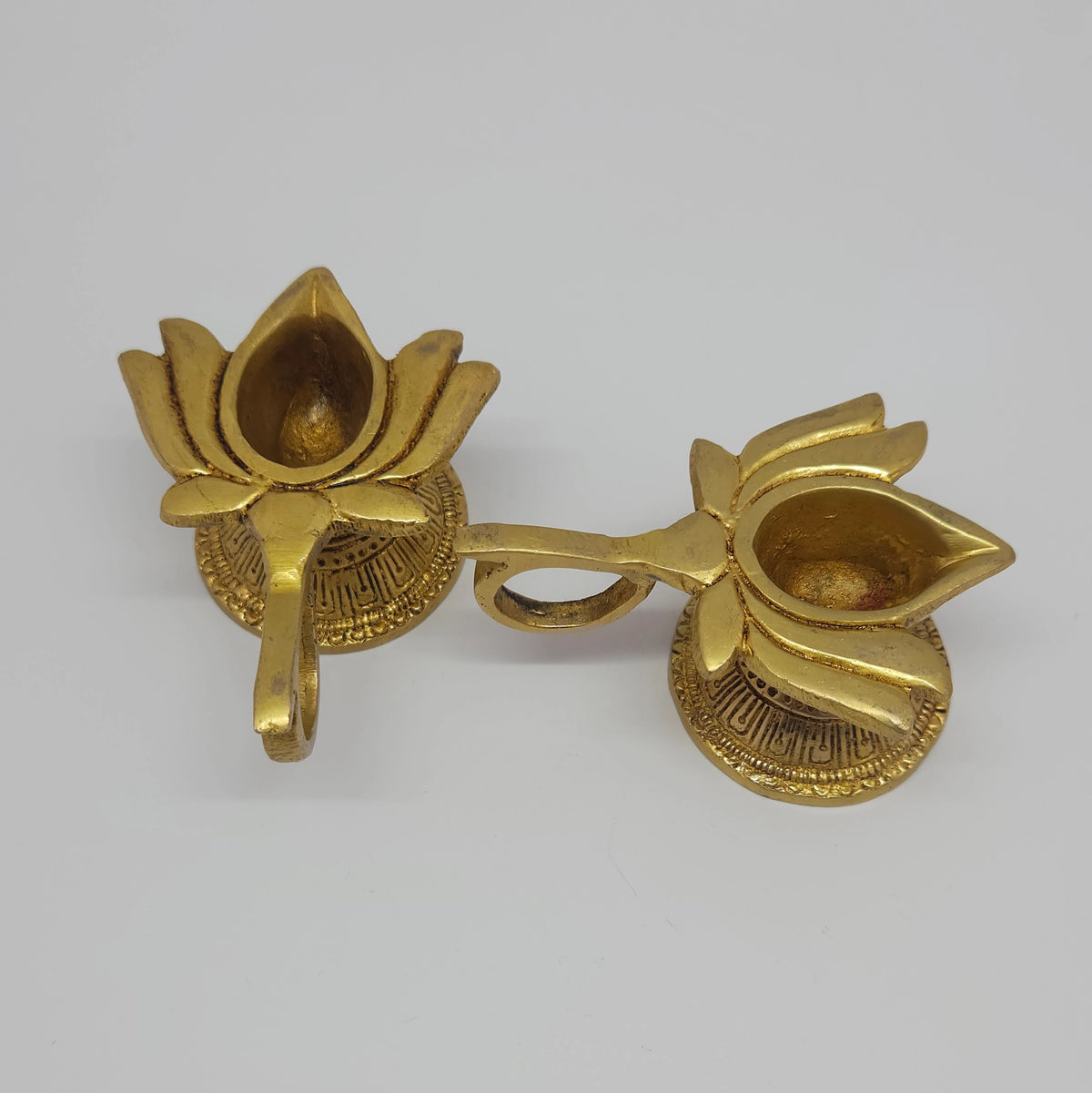 Display arrangement demonstrating two individual ten milliliter brass lotus handled lamps with one tilted forward to show the inner basin and wick placement groove.