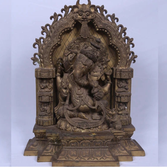 An antique bronze sculpture of Vinayakar, the Hindu god of wisdom, seated on a throne with intricate carvings and a serpentine figure beside it.