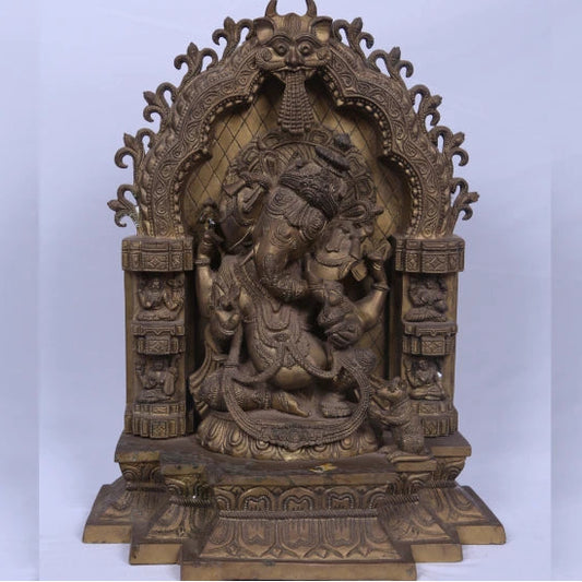 An antique bronze sculpture of Vinayakar, the Hindu god of wisdom, seated on a throne with intricate carvings and a serpentine figure beside it.