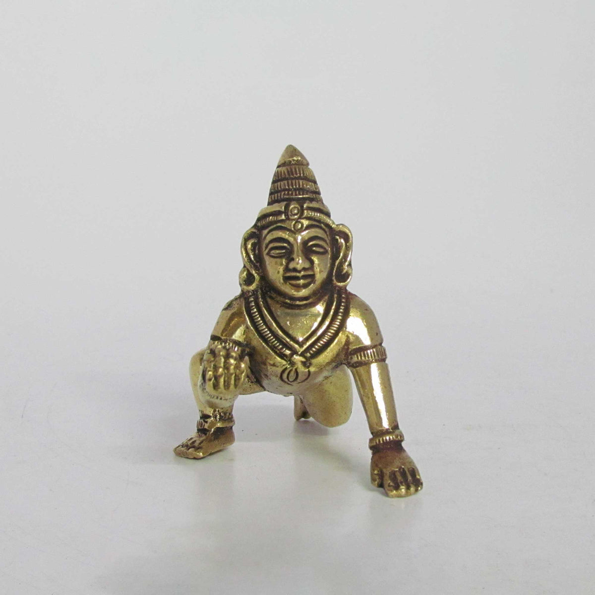 Direct front view of an antique finish brass crawling Bal Krishna idol, showcasing the facial features and traditional crown.
