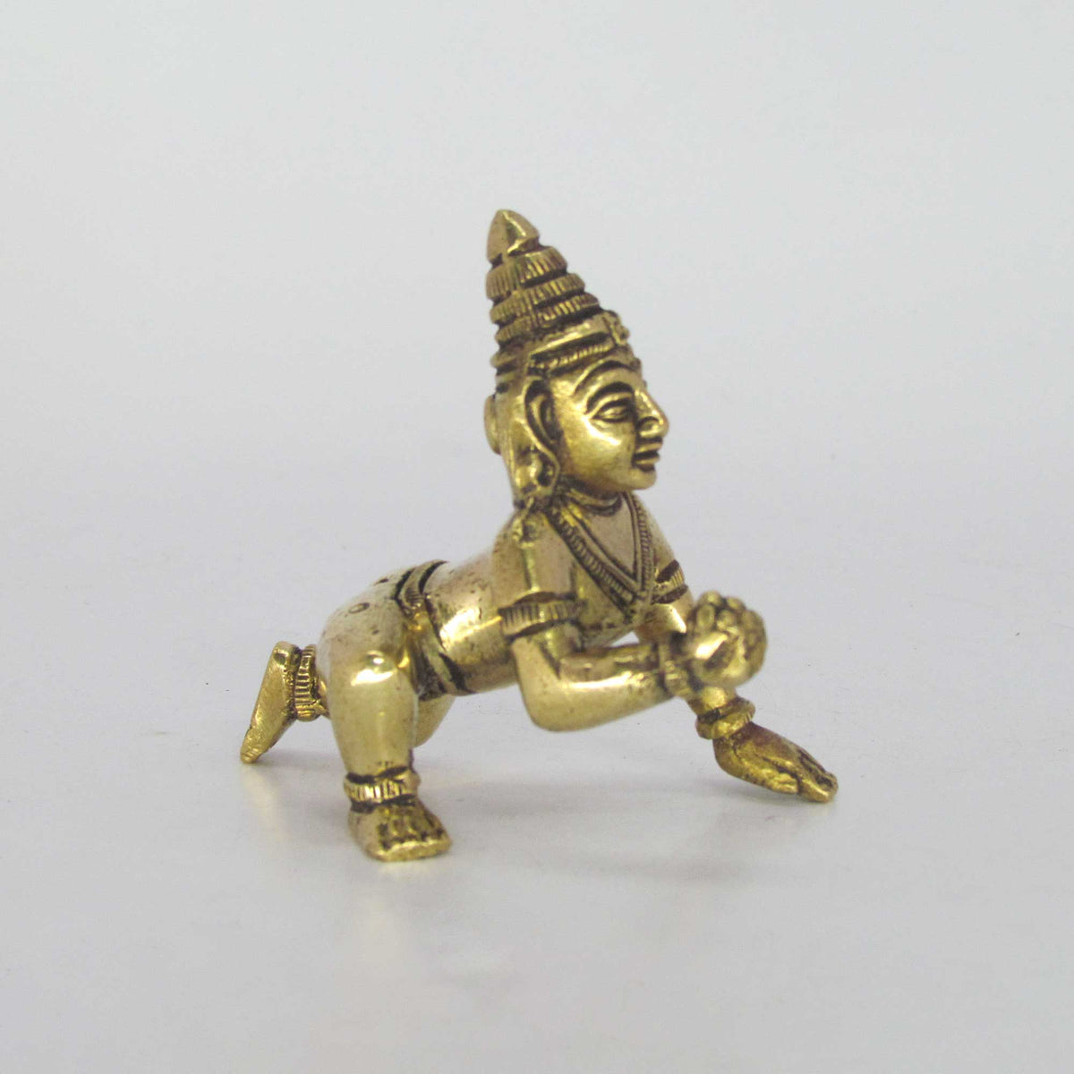 Three-quarter angle view of a solid brass crawling baby Krishna idol with a hand-rubbed antique patina finish, suitable for abishegam.