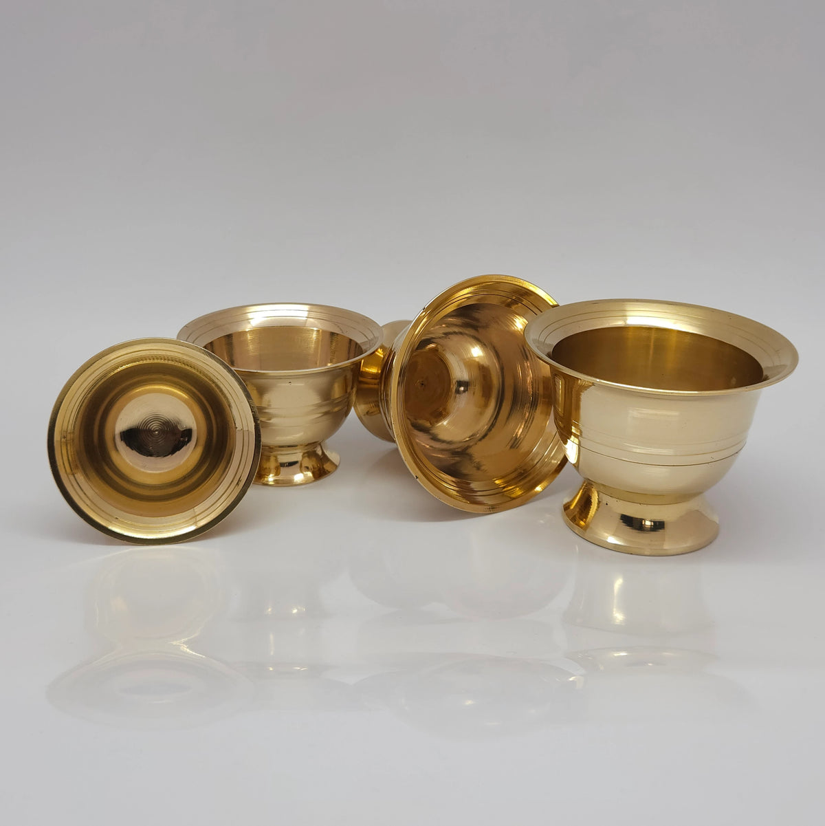 Group layout featuring one overturned brass chandan katori showing the hollow pedestal base cavity alongside other upright sandhanam ginni cups