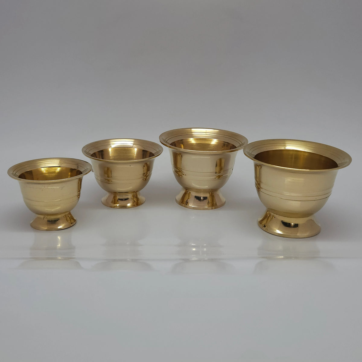 Side perspective arrangement of four pure brass chandana battalu cups lined up to showcase the gradual step down size variations.
