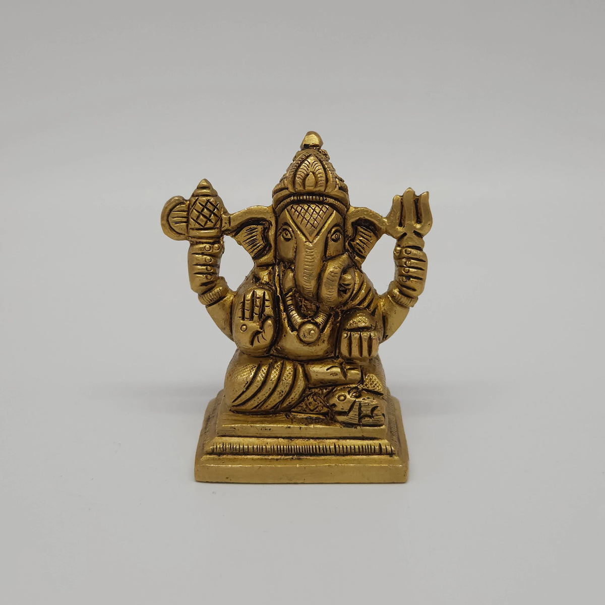 Straight close-up center shot of the antique finish brass Ganesha statue showcasing the detailed Trishula weapon, battle axe emblem, and seated Lalitasana posture.