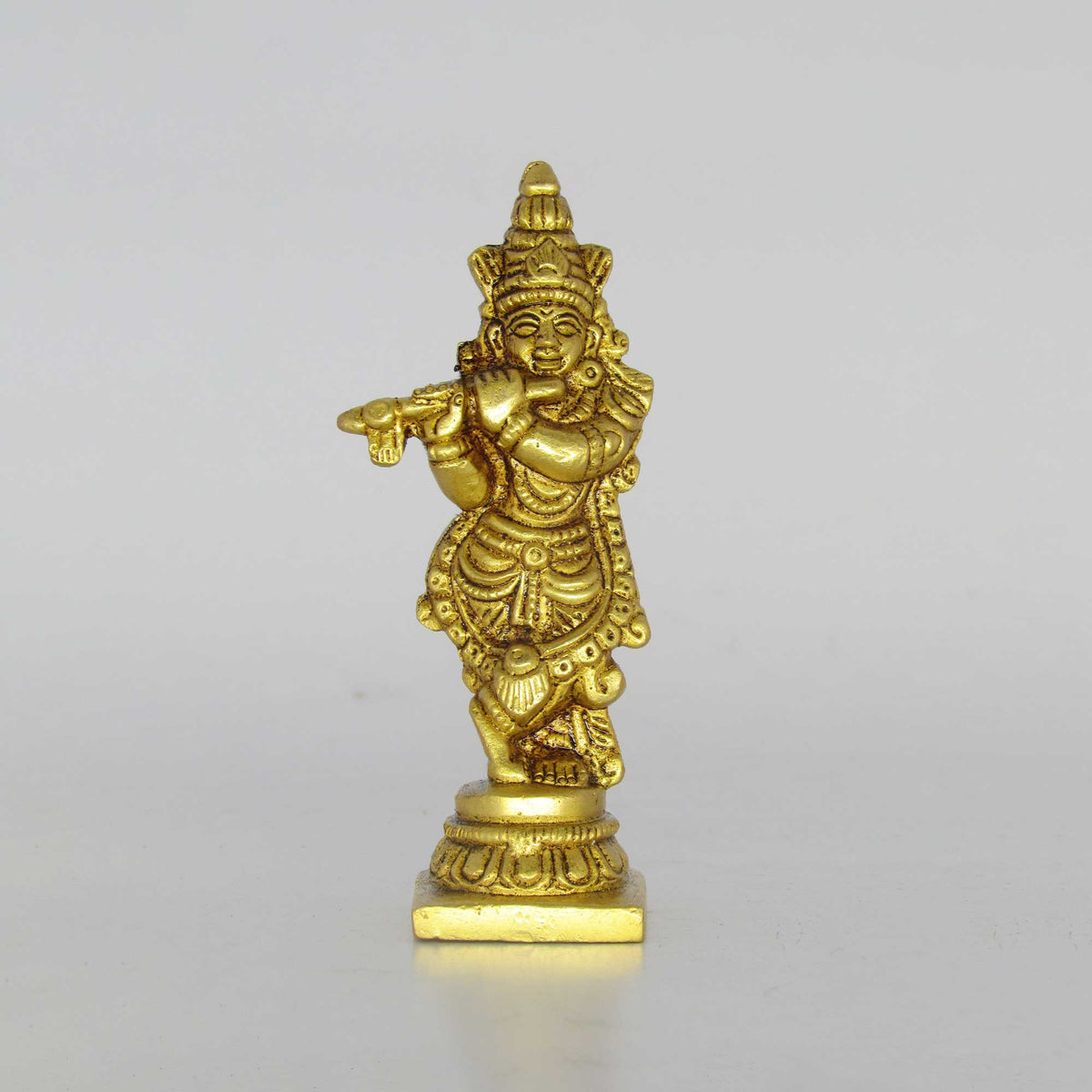 Direct front profile view of a pure brass fluting Krishna idol in tribhanga pose playing bansuri on a circular lotus base pedestal.