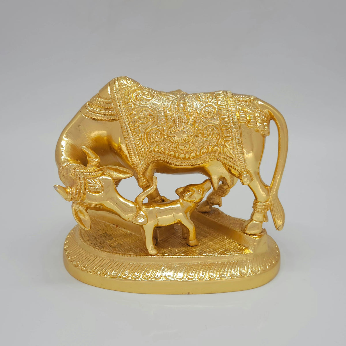 Direct front view of a 2.25kg glossy gold coated brass Kamadhenu cow statue gently bowing her head to lick her calf with loving care.
