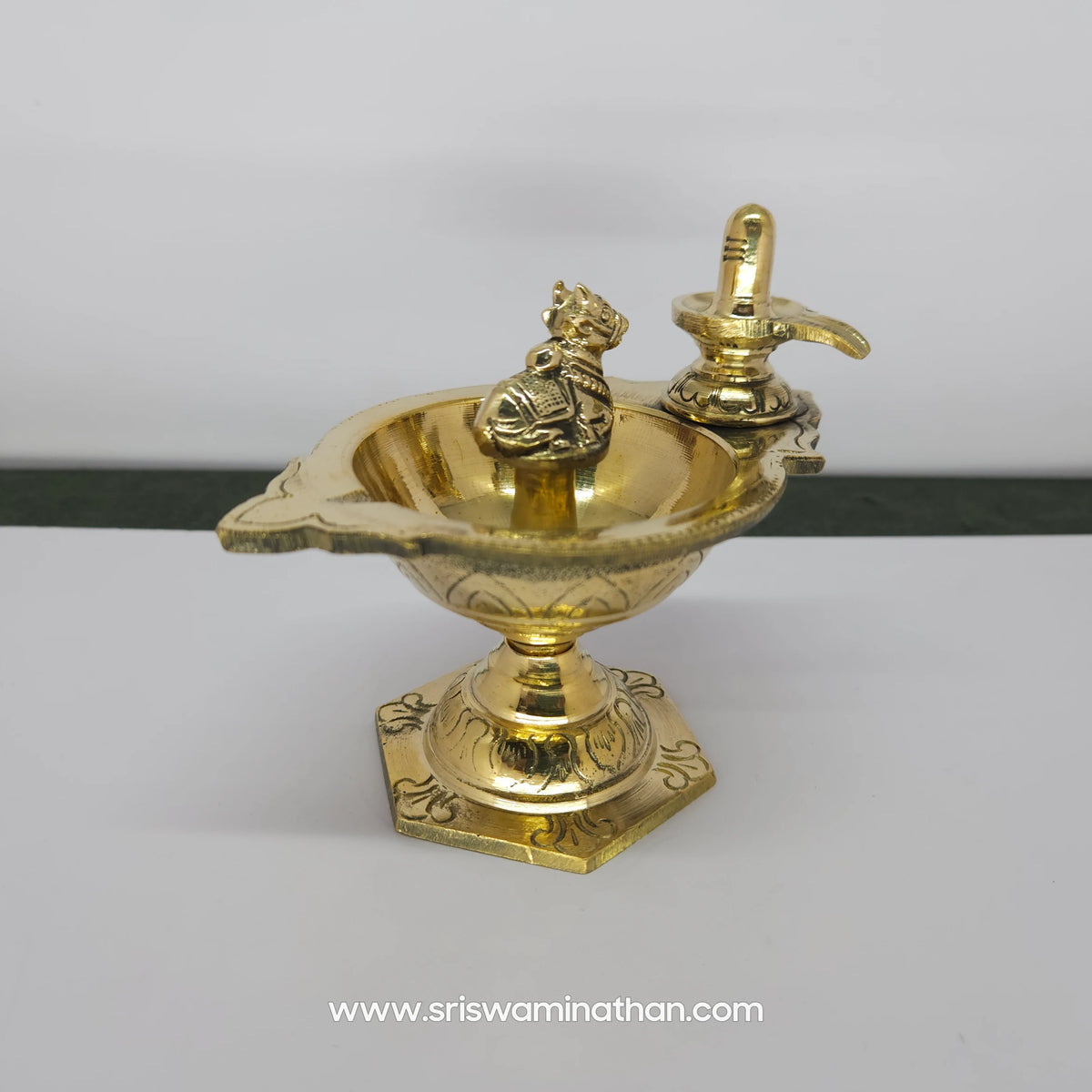 Direct front view looking down into the brass pradosham vilakku oil lamp bowl, showing the seated Nandi facing the sacred Shiva Lingam.