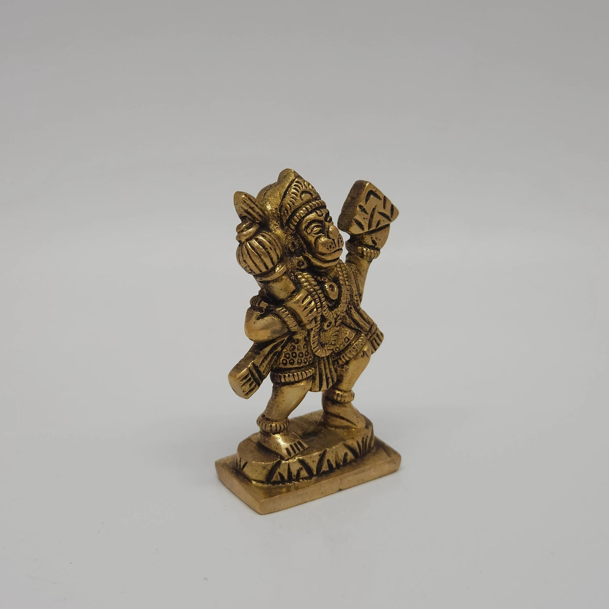 Three-quarter front right perspective view of the solid brass Hanuman statue focusing on the physical relief of the Sanjeevi mountain held aloft and the Gada details