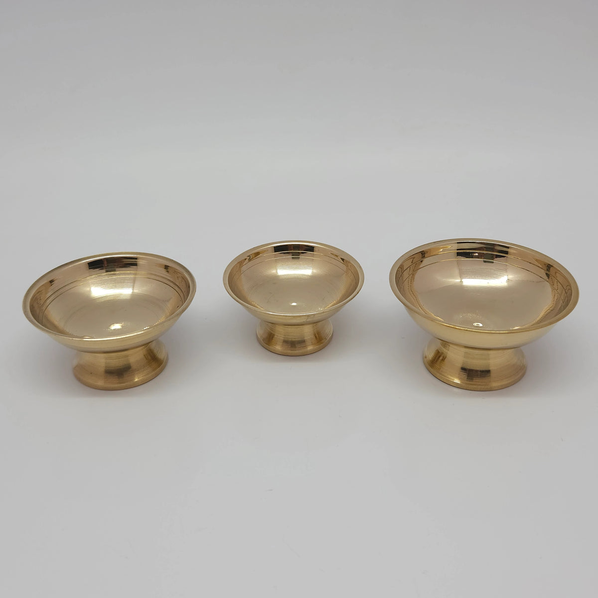 High angle perspective view of the three pure brass offering bowls showing the depth of the shallow cups and consistent golden tone.