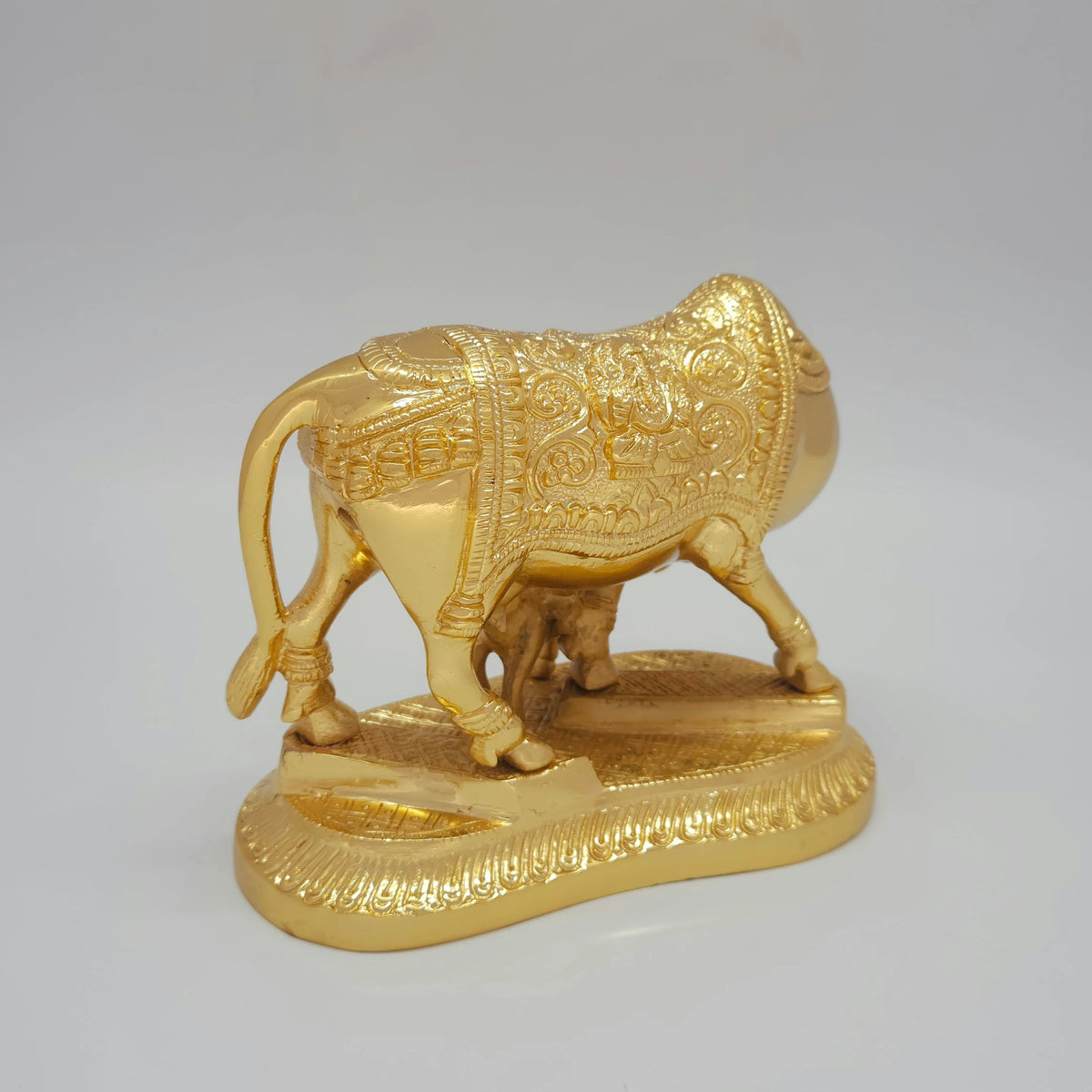 Right profile view of the heavy brass cow and calf statue showcasing the detailed Lord Ganesha engraving on the back side of the cloth carpet.
