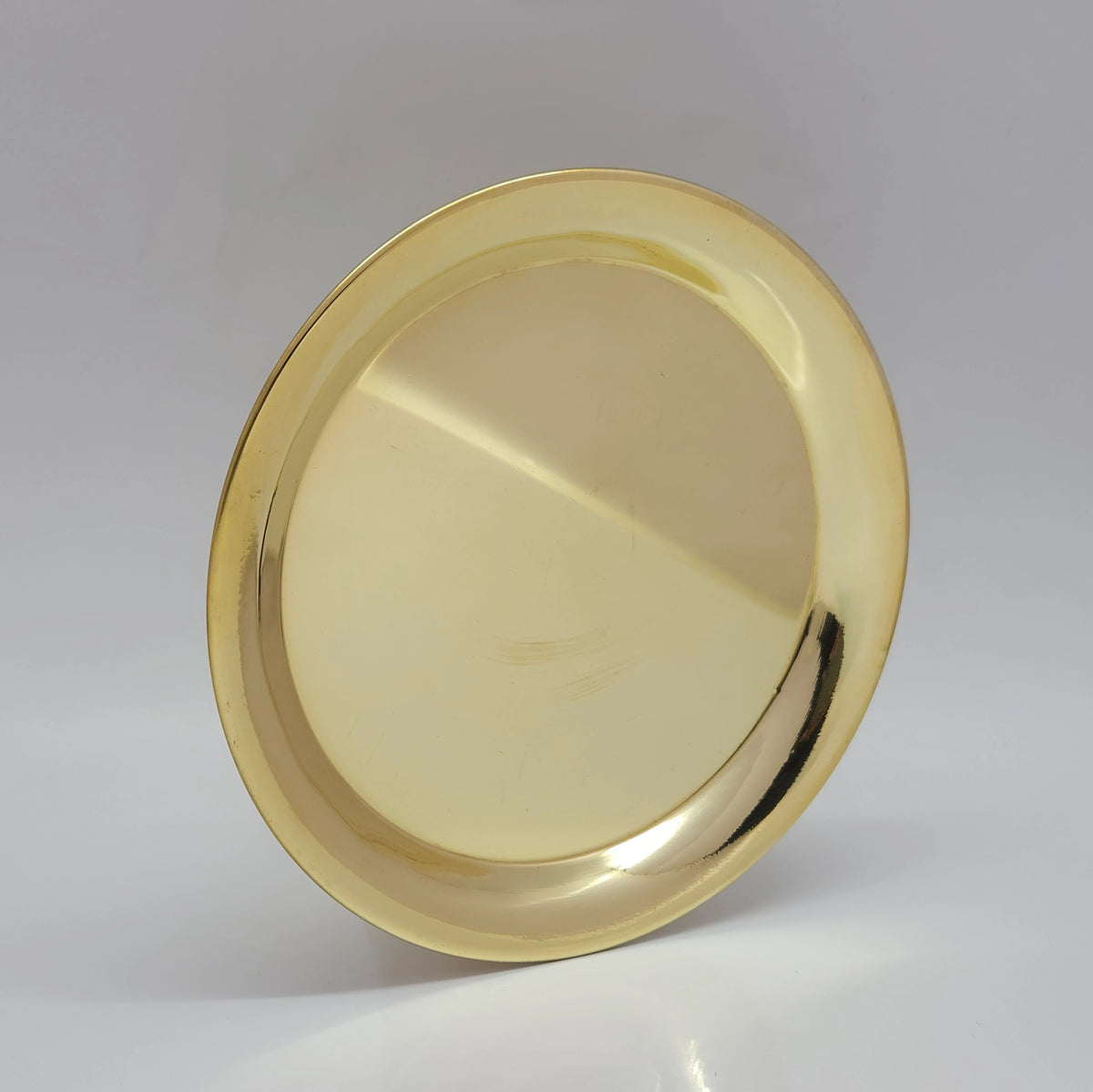 Three-quarter tilted perspective view of pure brass plain plate showcasing the shallow basin depth and structural outer rim.
