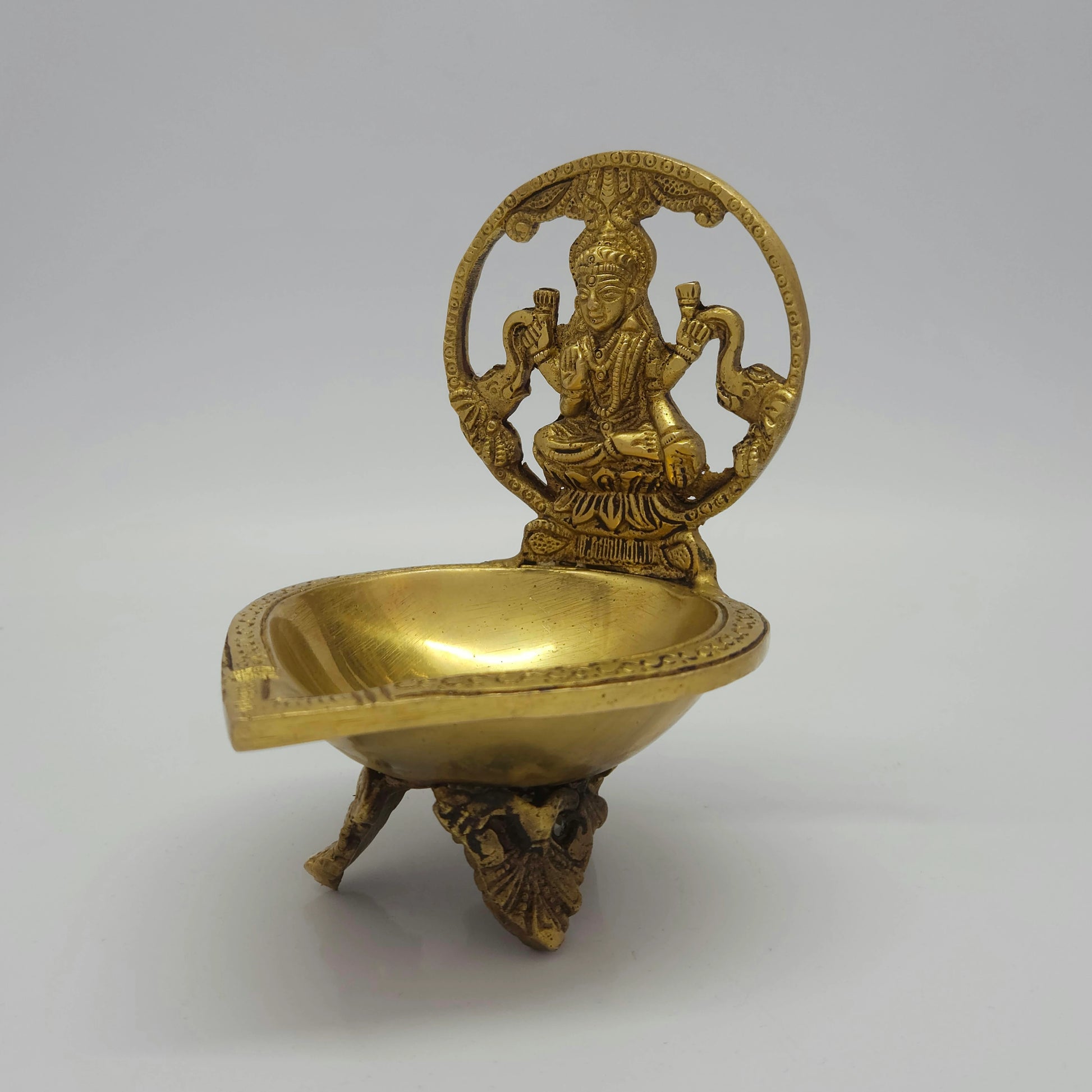 Front-left 45-degree angle profile view highlighting the elephant abhishekam arch details, deep oil bowl cavity, and lion pedestal feet