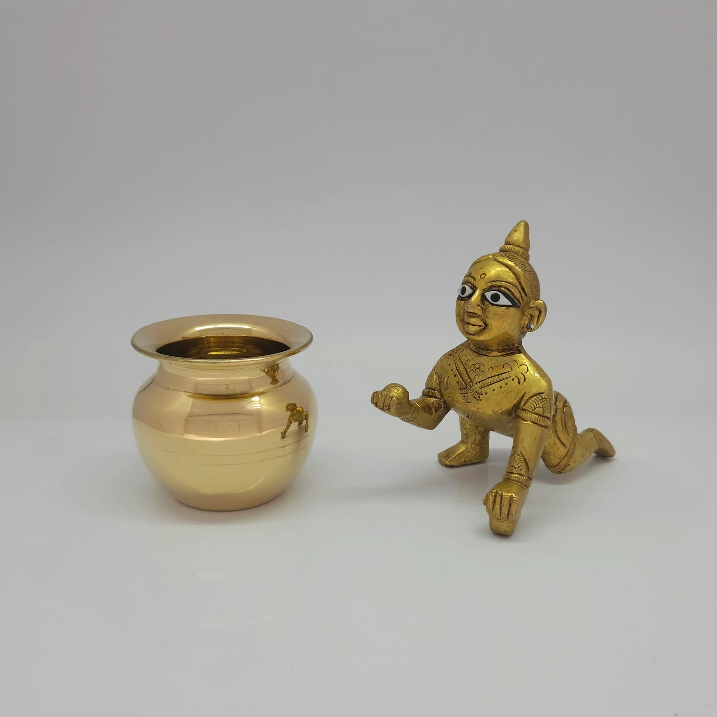 Flat straight front view of the 9cm high antique solid brass crawling Laddu Gopal Bala Krishna statue sitting right next to his high-gloss companion brass butter pot