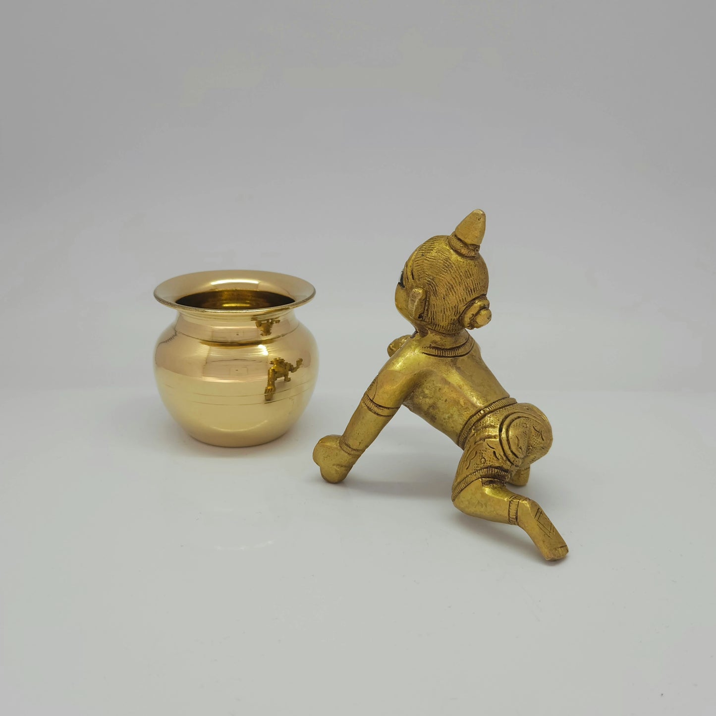 Rear-left 45-degree perspective view showcasing the solid back structure of the baby deity, waist chains, and rich deep metal antique shadow lines