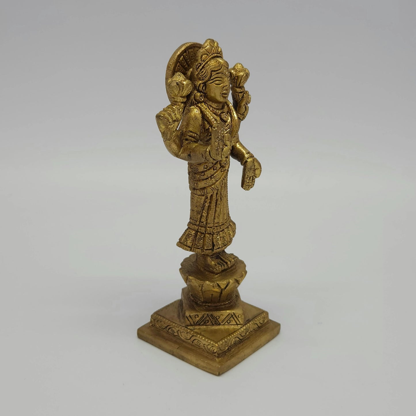 Solo right 45-degree angle close-up of the antique solid brass Goddess Lakshmi idol focusing on the hand-rubbed temple shading along the saree folds and tiered base.