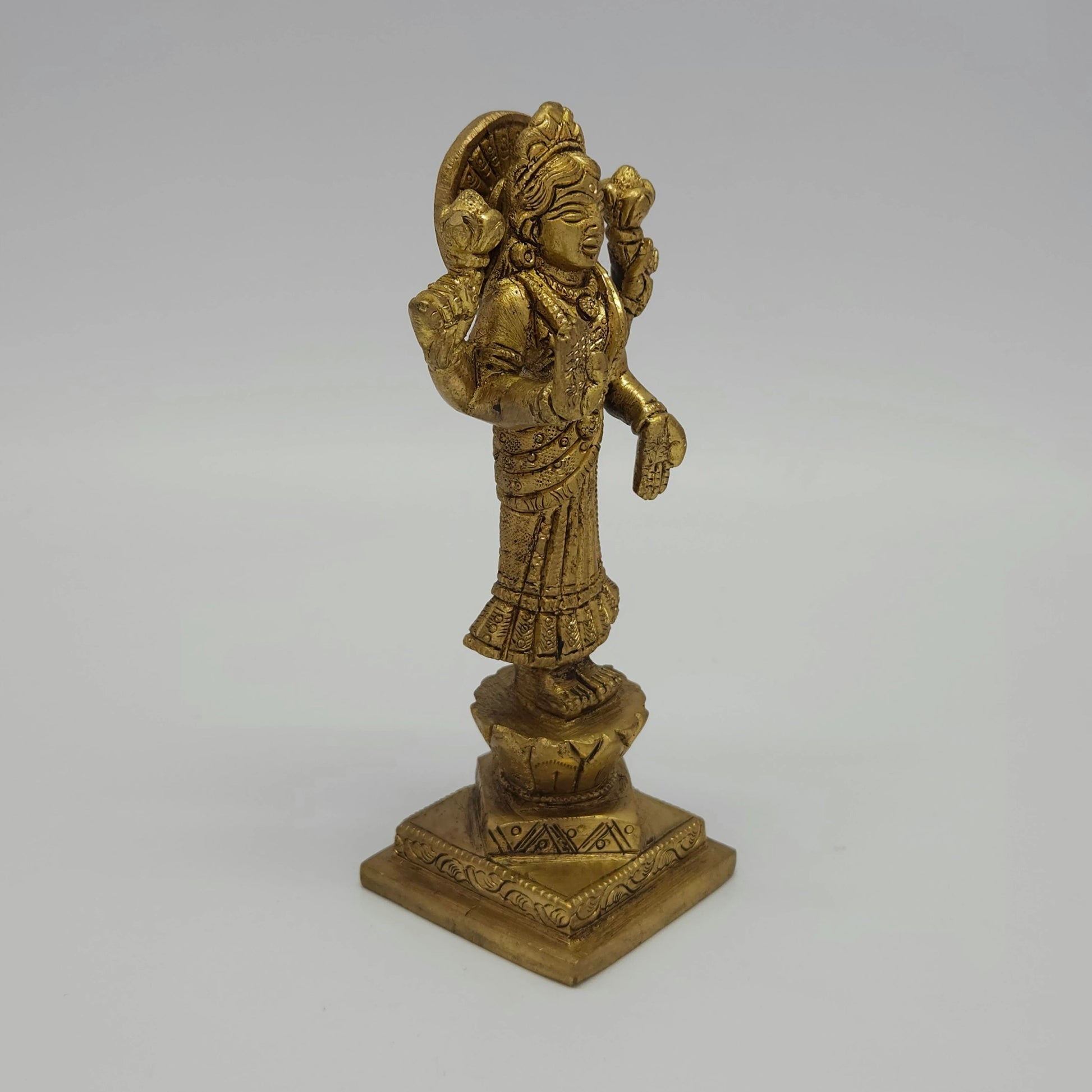 Solo right 45-degree angle close-up of the antique solid brass Goddess Lakshmi idol focusing on the hand-rubbed temple shading along the saree folds and tiered base.