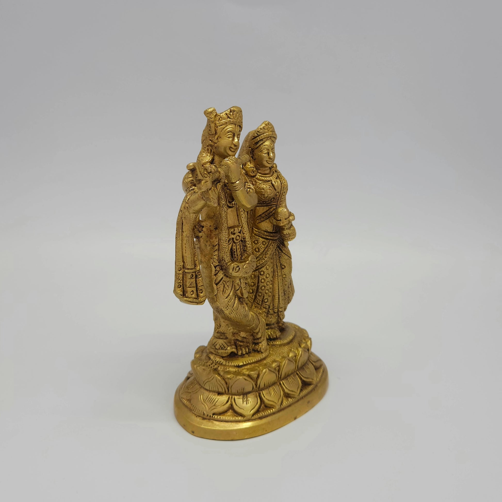 Front-right 45-degree angle profile view focusing on Goddess Radha's posture, hand-held lotus detail, and the flowing symmetry of the traditional vestments.