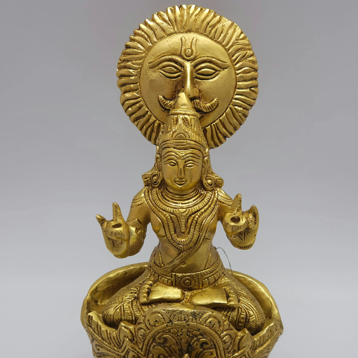 Close-up zoom perspective focusing on the serene facial features, traditional crown, mudra hand gestures, and hand-polished antique texture of Lord Surya.