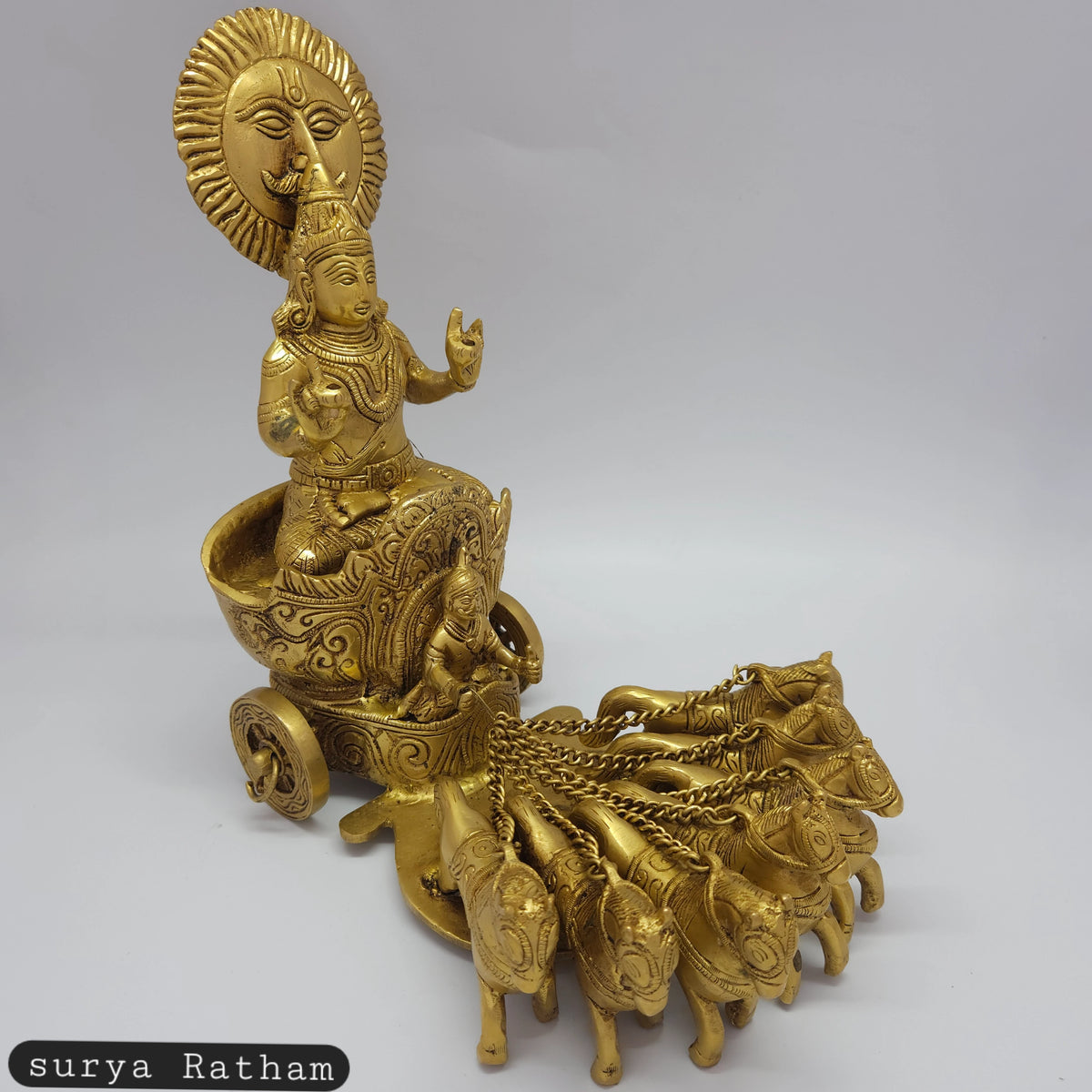 Front-right 45-degree angle view of the 18.5cm solid brass Surya Ratham statue showing the sunburst halo, seven horses, and detailed chariot tire.