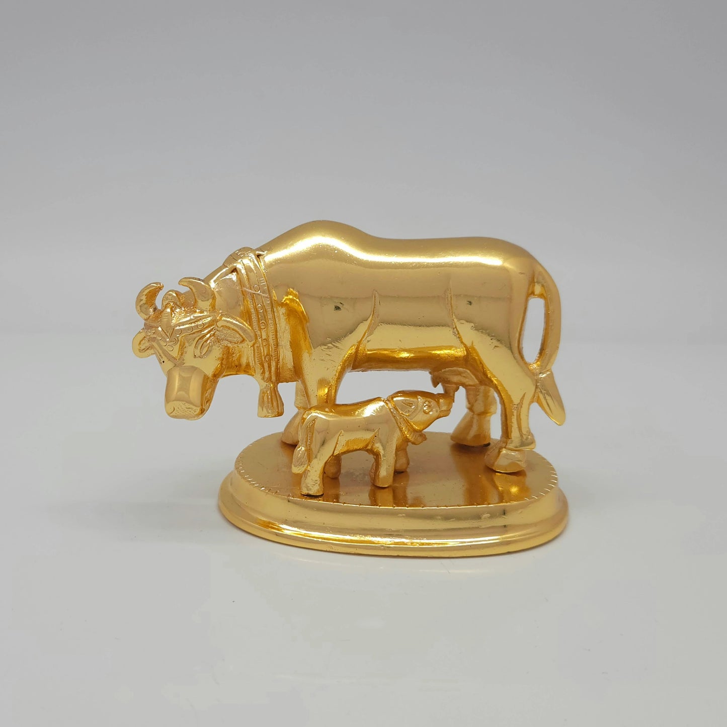 Flat straight front view of the 7cm compact high-gloss satin gold brass Kamadhenu cow and calf statue on a circular base