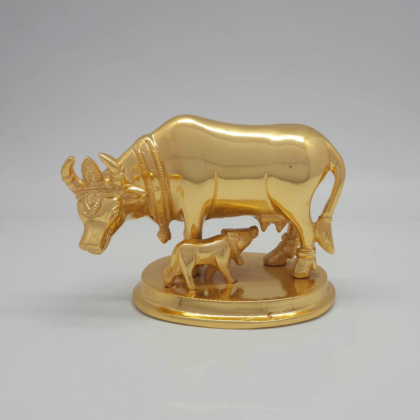 Flat straight front view of the premium high-gloss satin gold brass Kamadhenu cow and calf statue showing the ornate crown carvings