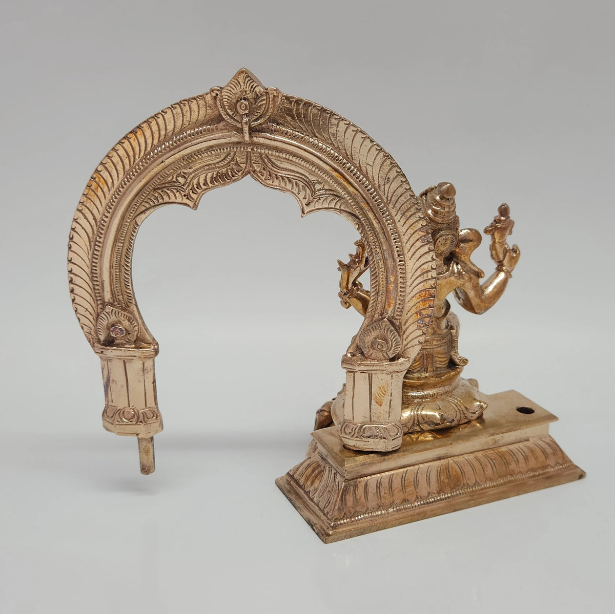 Side angle demonstration showing the traditional Prabhavali archway being pulled upward and out from the rear base mounting slots of the solid metal Ganesha idol.