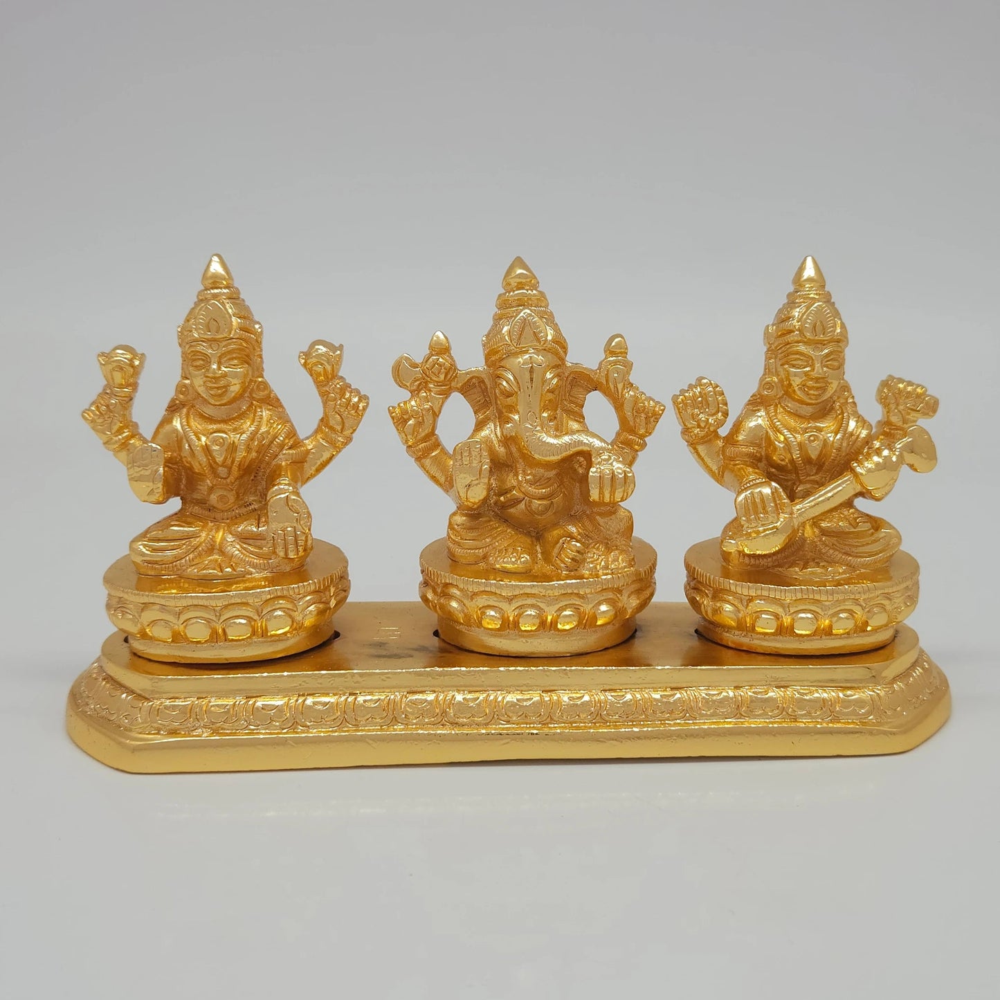 Front view of the 8cm premium gold powder-coated brass Laxmi Ganesha Saraswati trinity on an elongated platform for office front desk decoration.