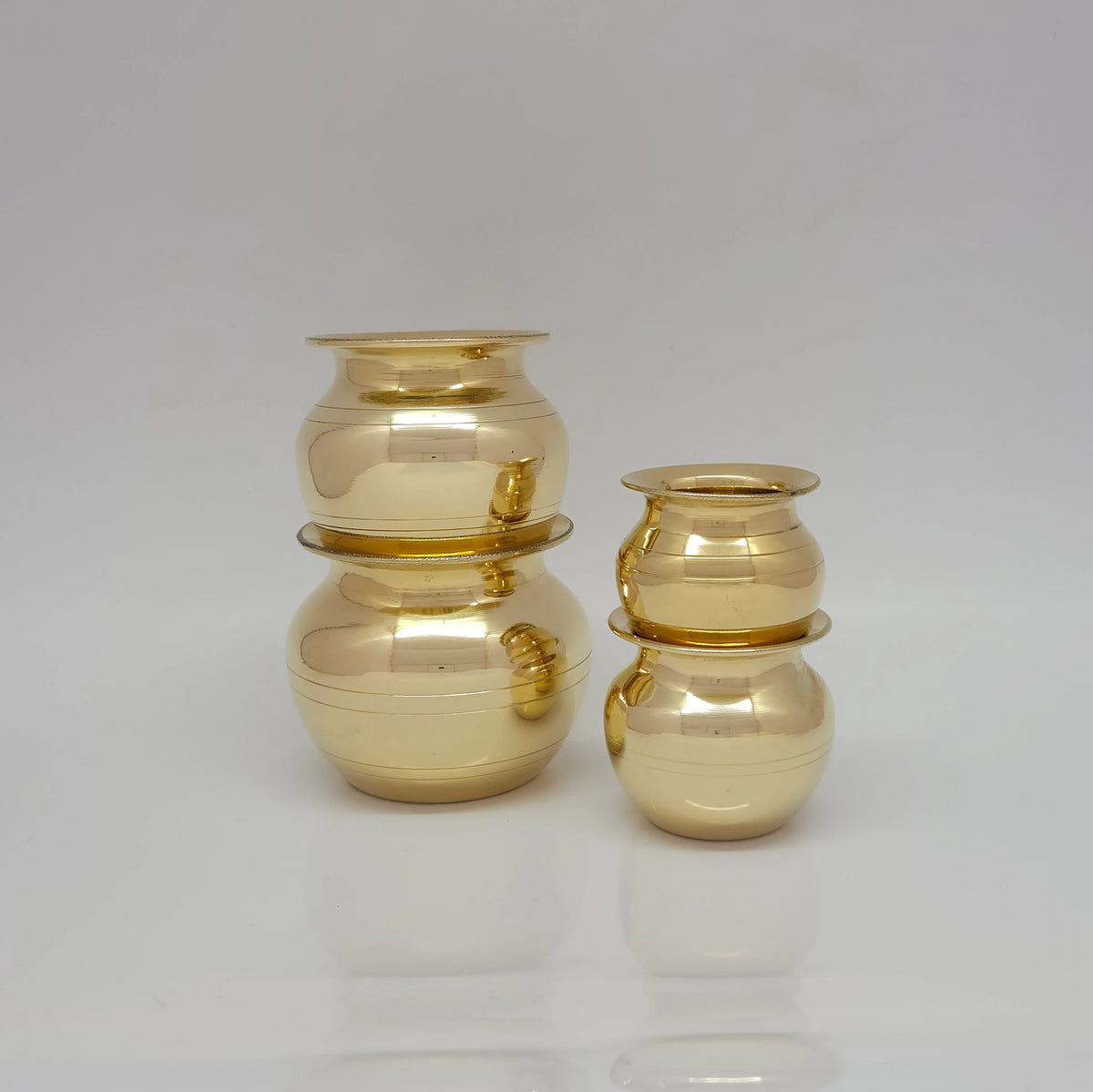 Wide shot of the four pure brass Kubera Panai pots arranged side by side in a straight horizontal line to demonstrate the gradual increase in height and volume