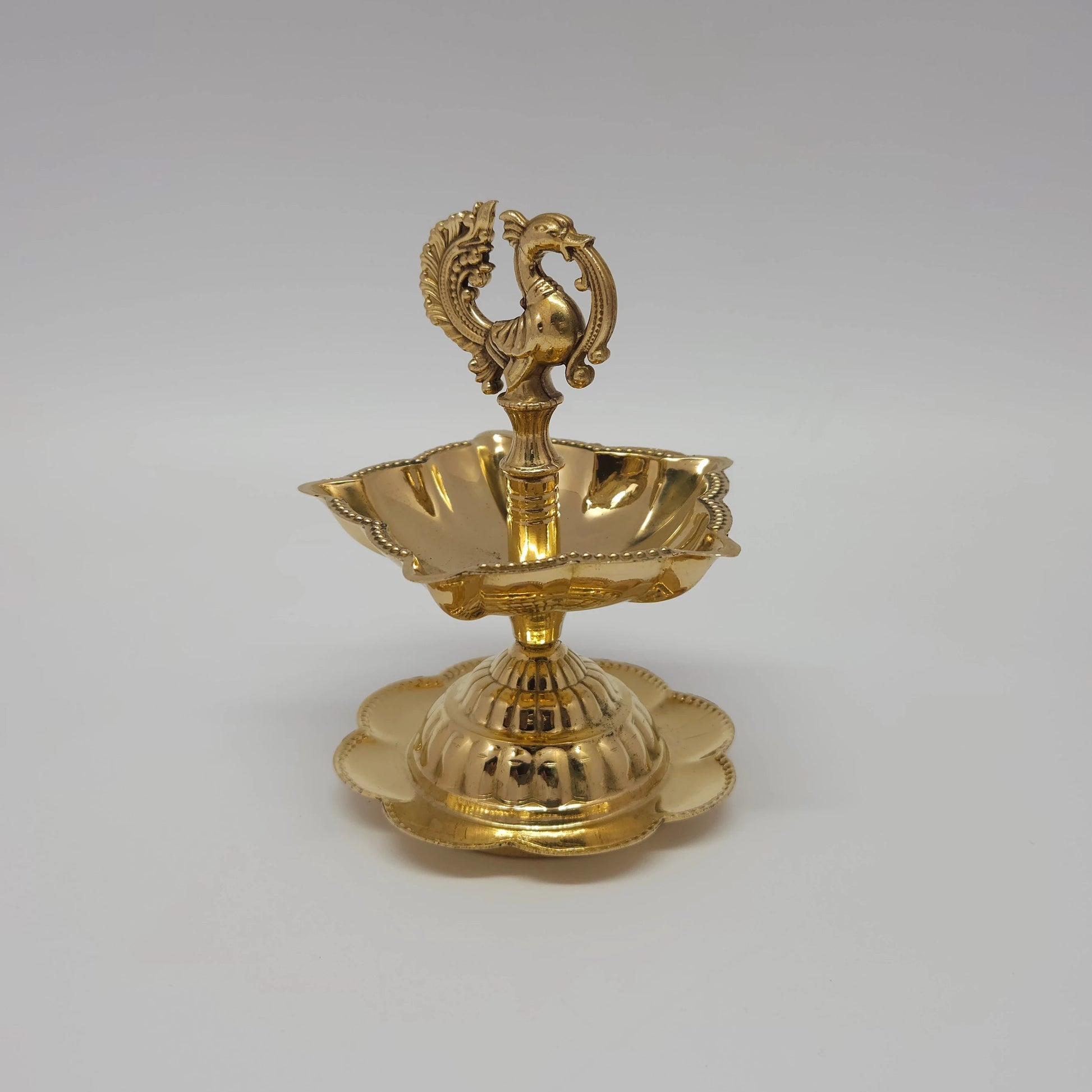 A single brass peacock lamp with five wicks and stable floral base.
