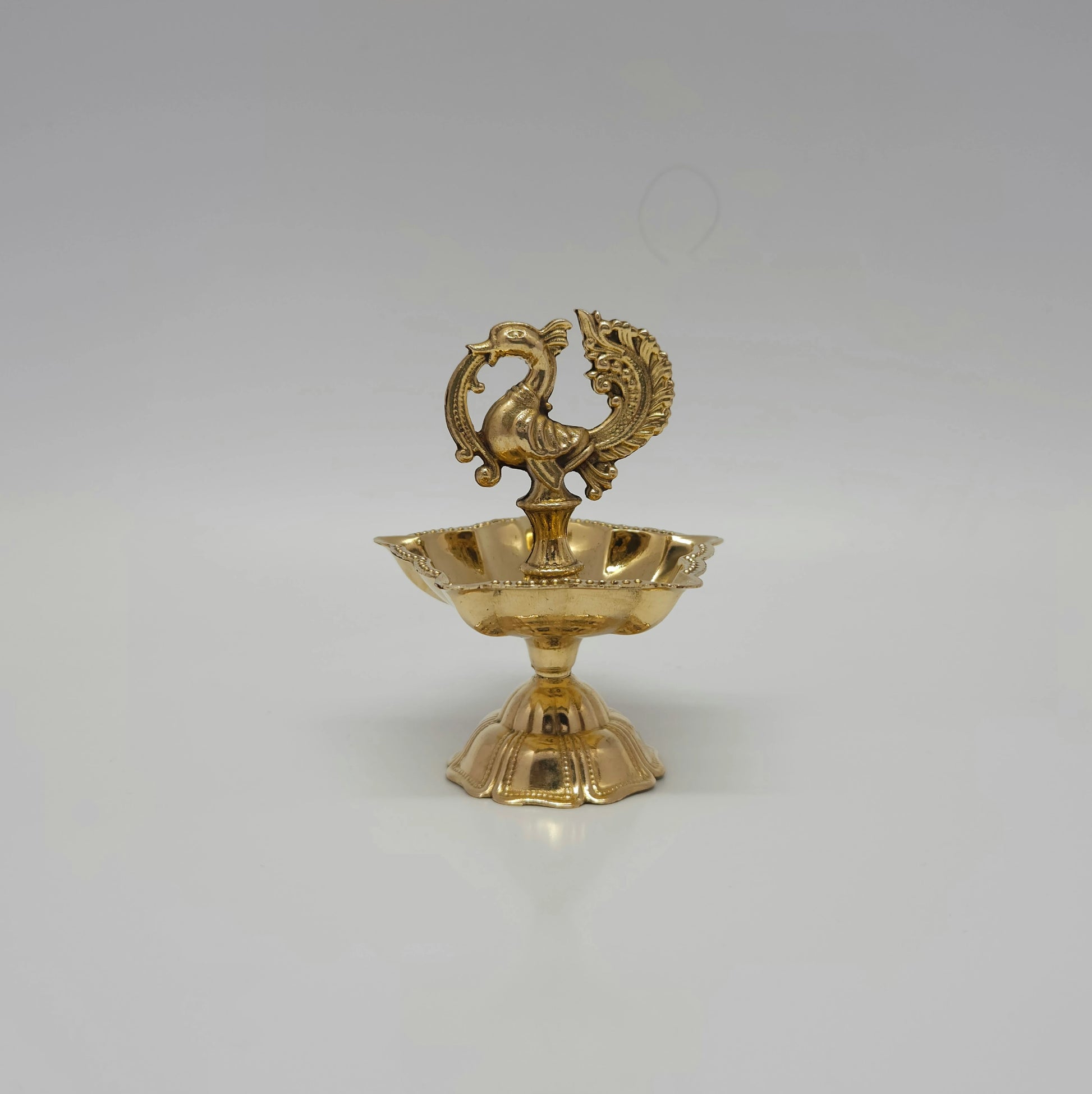 A single brass peacock lamp with five wicks for daily home prayers.