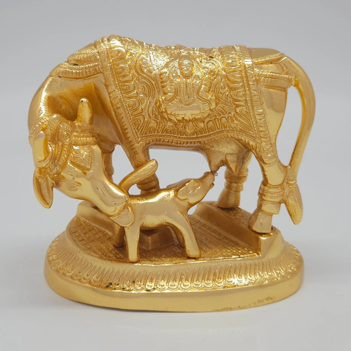 Front view of the 11cm premium gold powder-coated solid brass Kamadhenu cow and calf statue showing the nursing posture and Lakshmi engraving.