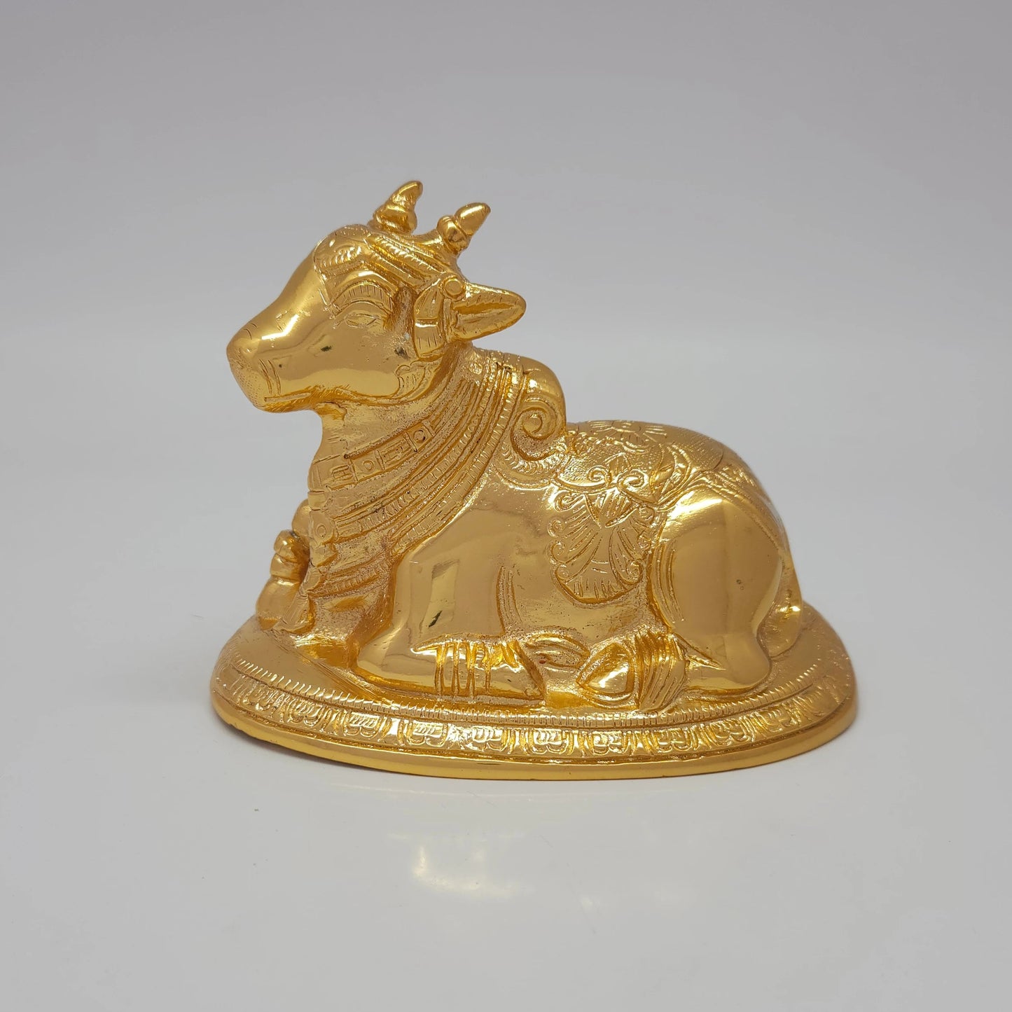 Profile front view of the 13.5cm premium gold powder-coated hollow brass reclining Nandi sculpture with intricate neck bells.