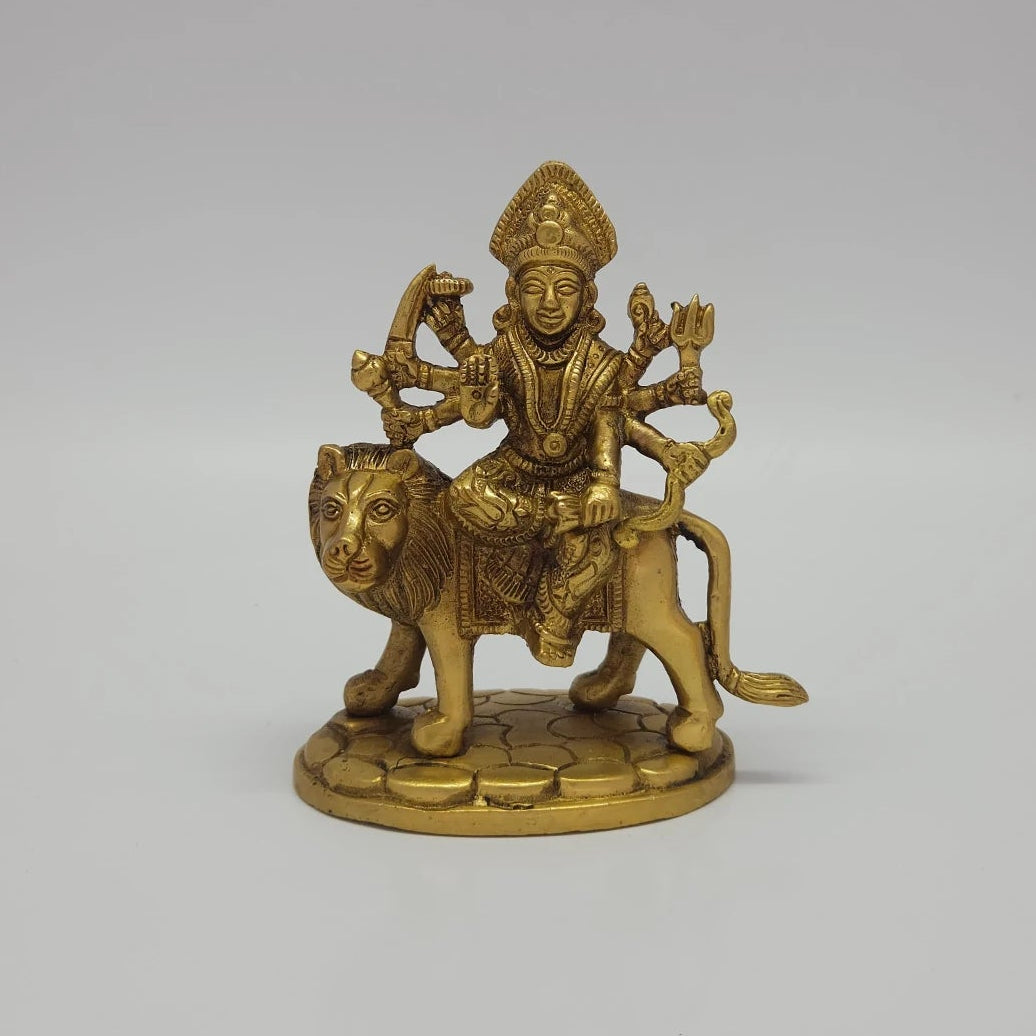 Front view of the 13cm antique solid brass Simhavahini Durga statue with eight arms holding weapons on a textured oval base for Navaratri puja