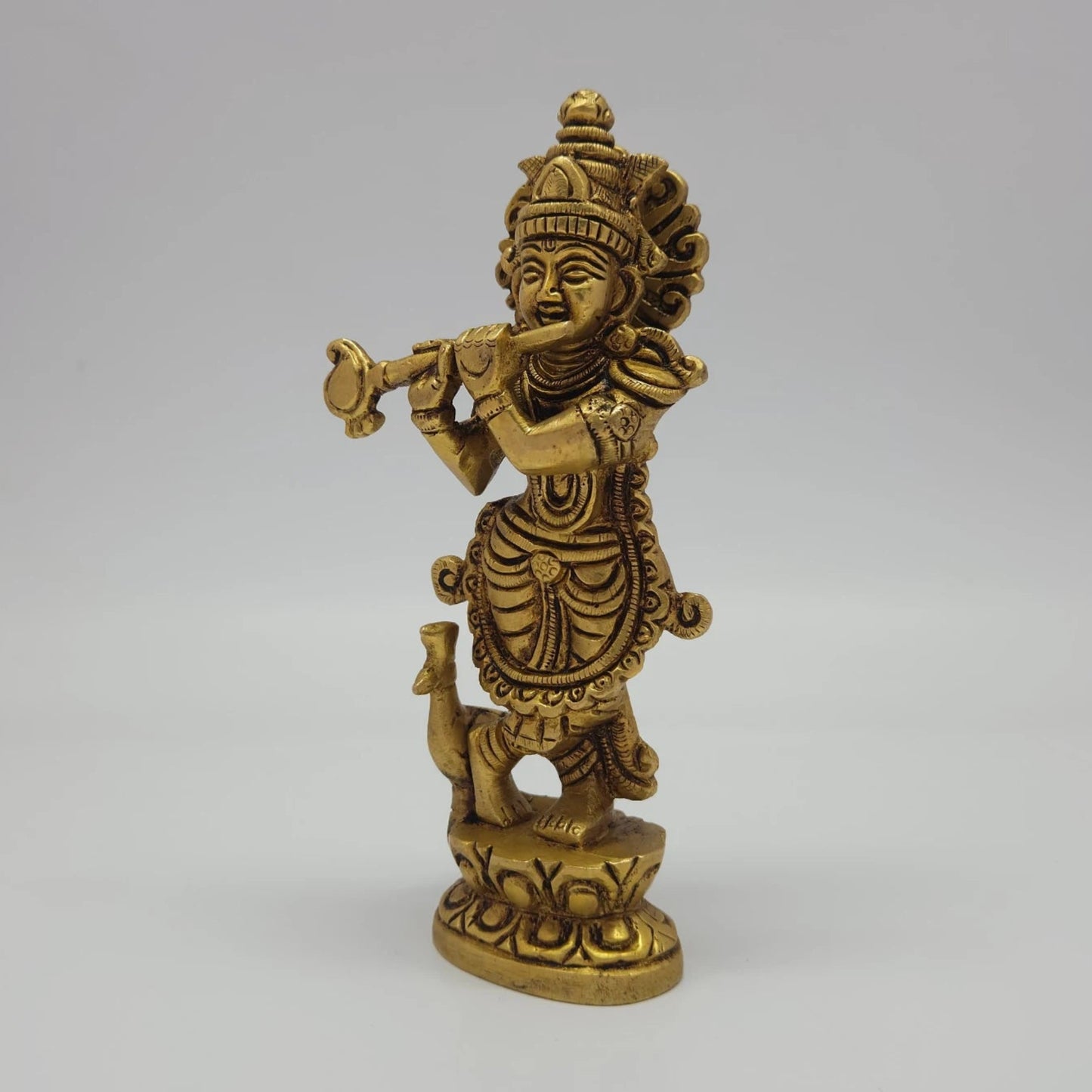 Left 45-degree angle profile emphasizing Krishna's three-bend posture, arm placement, and the finely detailed peacock companion.