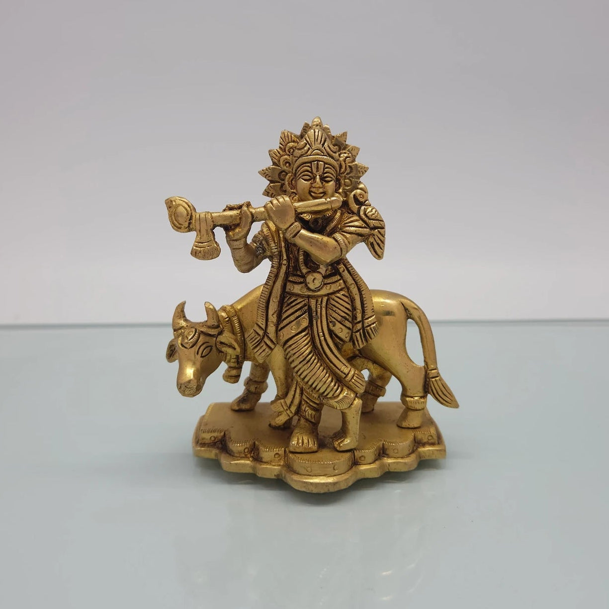 Front view of the 12cm antique solid brass cross-legged Muralidhar Krishna statue with flute and cow on a lotus cloud base for Janmashtami puja.