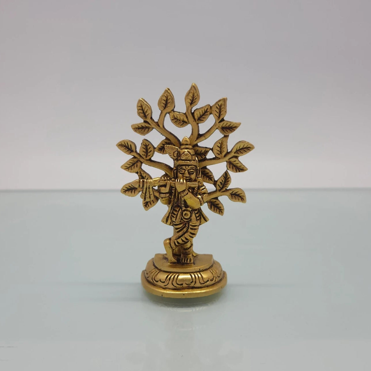 Front view of the 9.5cm antique solid brass cross-legged Balakrishna statue playing flute under a Kadamba tree for Janmashtami pooja.
