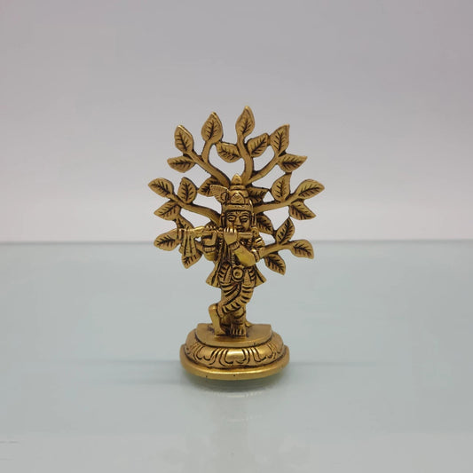 Front view of the 9.5cm antique solid brass cross-legged Balakrishna statue playing flute under a Kadamba tree for Janmashtami pooja.