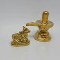 Low angle side profile view of the 3.5 inch brass Shivling showing the long drainage spout of the yoni tray next to the seated Nandi bull.
