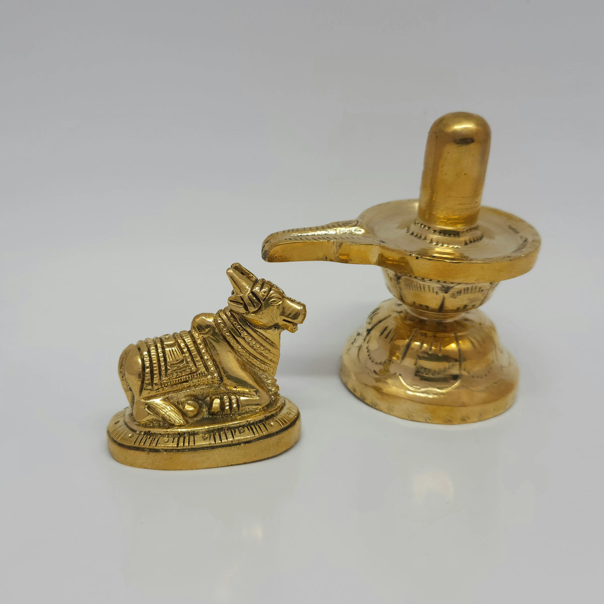 Low angle side profile view of the 3.5 inch brass Shivling showing the long drainage spout of the yoni tray next to the seated Nandi bull.