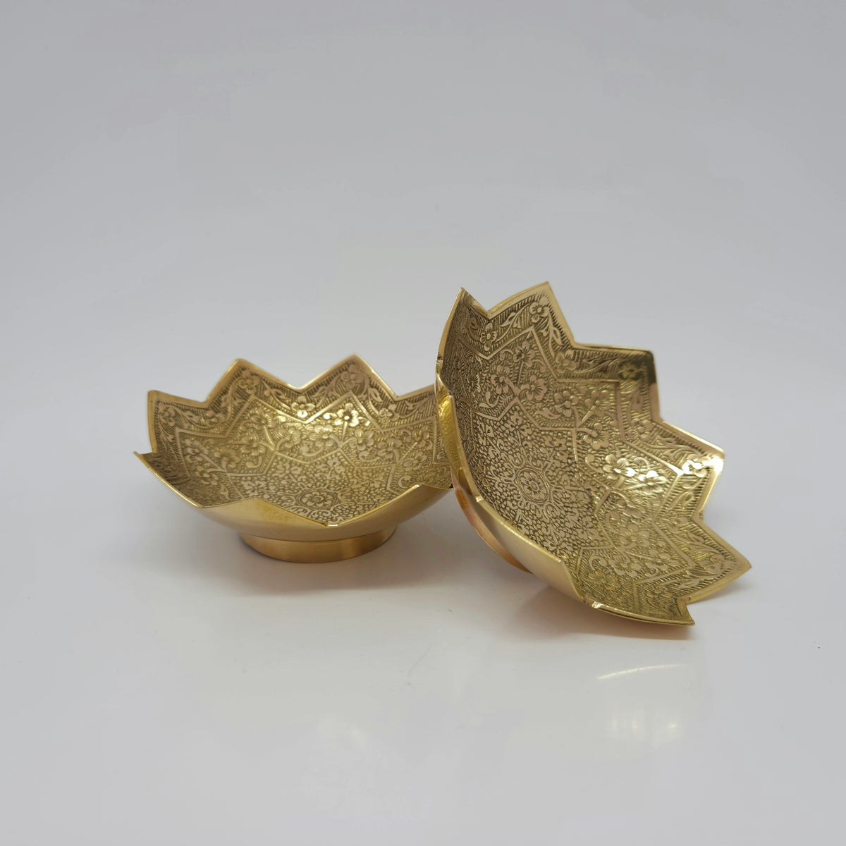 Three-quarter perspective view displaying one 4 inch lotus brass bowl standing upright next to another tilted forward to reveal the detailed interior crown carvings.
