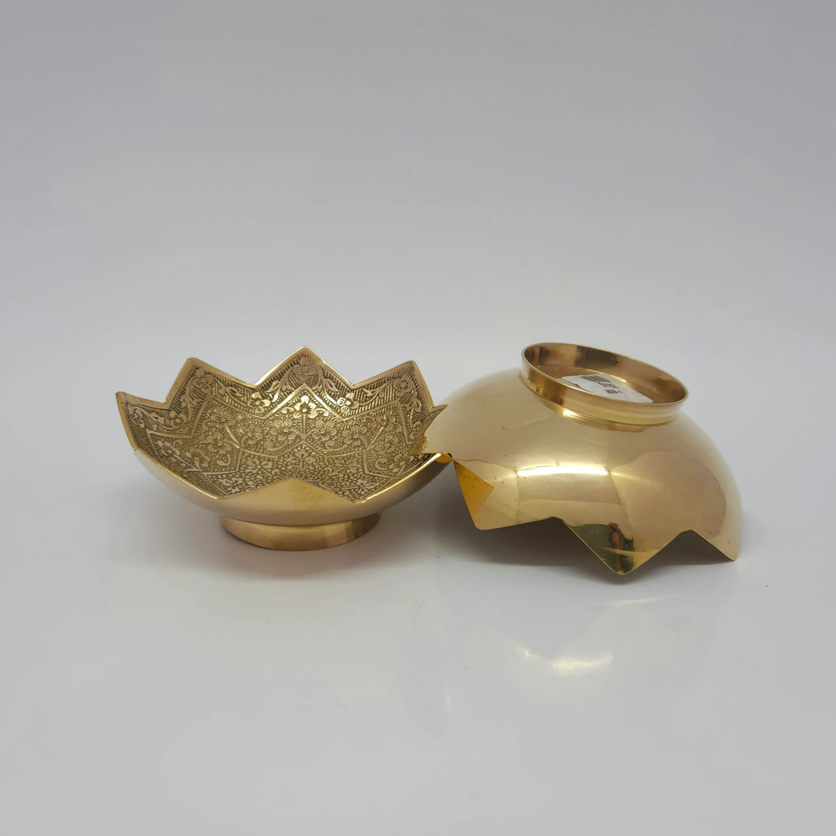 Angled view displaying one 4 inch lotus brass bowl standing upright next to another bowl resting face down to reveal the smooth round pedestal base design.