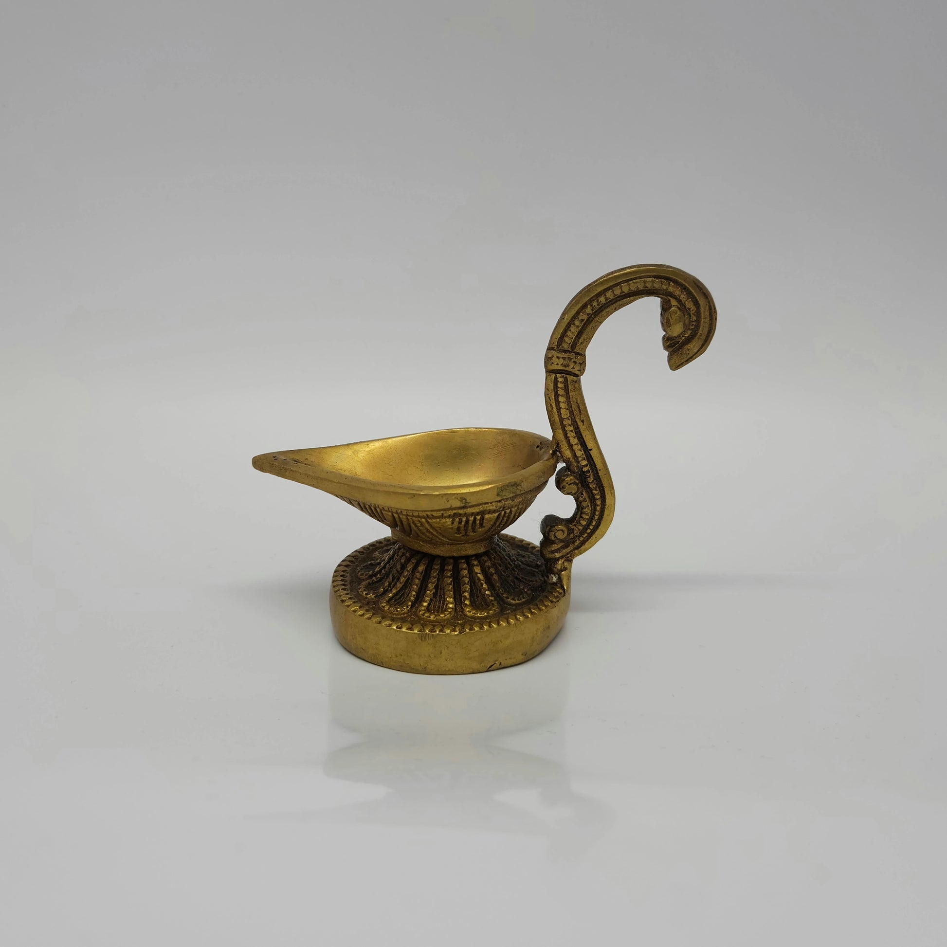 Side profile view of the 13cm antique brass handheld aarti diya showing the curved swan handle facing left by Sri Swaminathan and Co