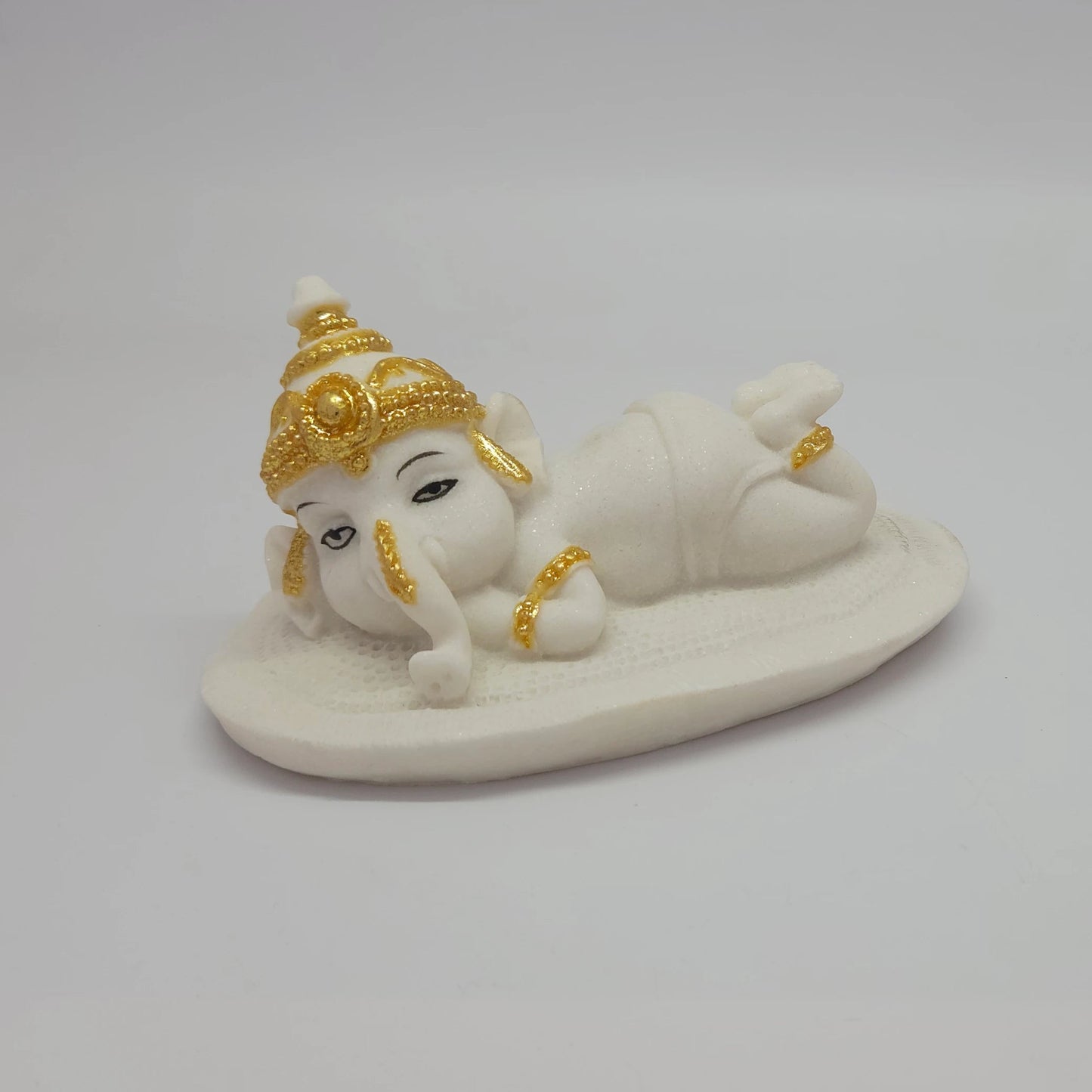Three-quarter front view of the white poly-marble child Ganesha figurine showcasing his peaceful hand-painted facial features.