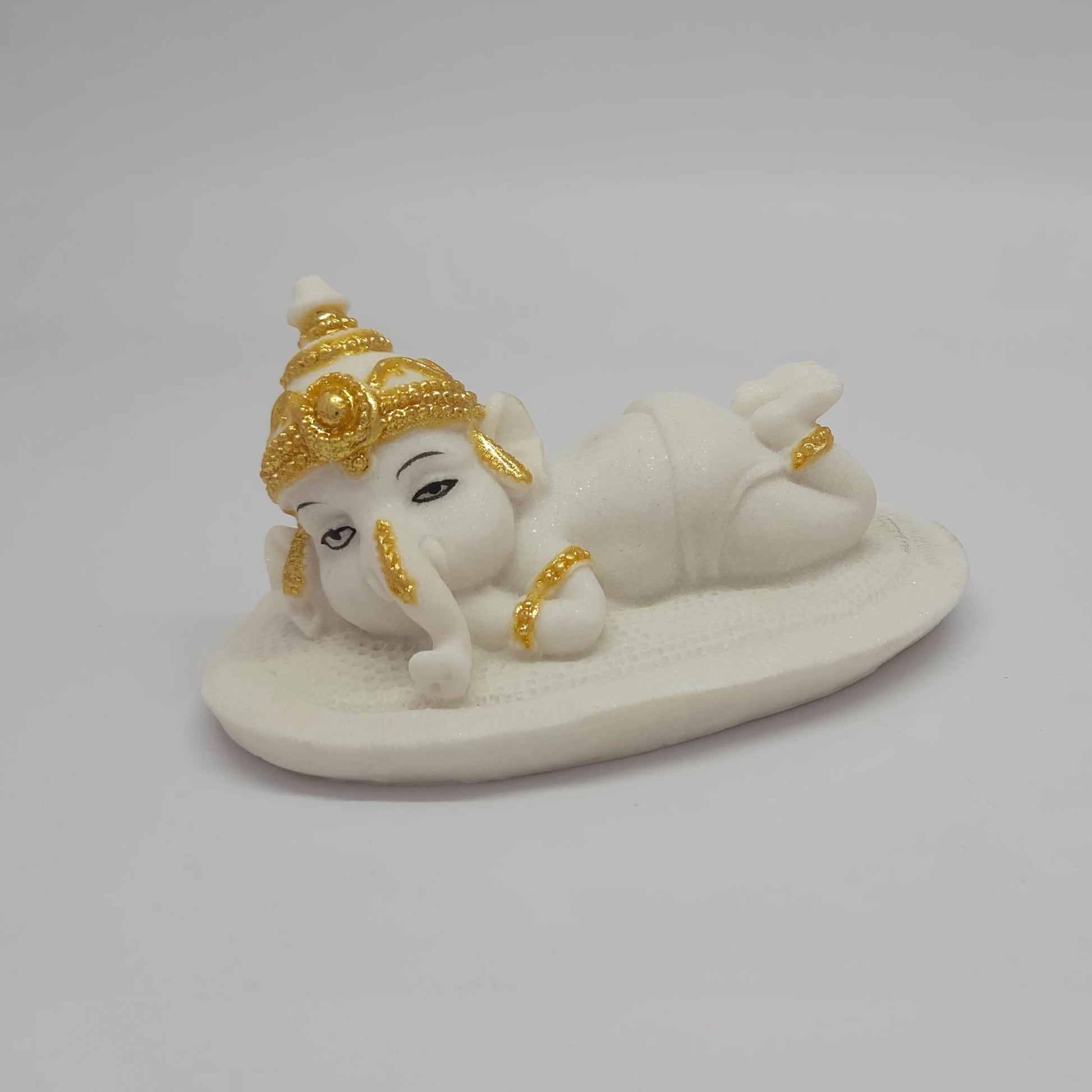 Three-quarter front view of the white poly-marble child Ganesha figurine showcasing his peaceful hand-painted facial features.