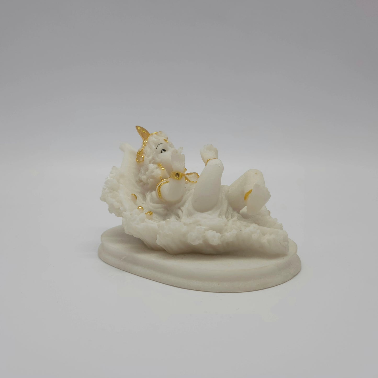 Angled back left view of the reclining baby Krishna sculpture showing his posture on the leaf bed and the sturdy oval base plate.